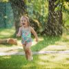The little baby girl playing with garden sprinkler. Summer outdoor water fun and green grass.